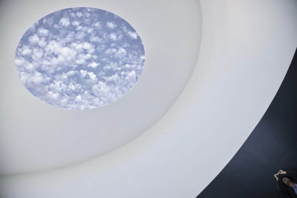 “Skyspace” is an art installation consisting of a white, circular enclosure with an oval shaped opening in the ceiling, allowing the sky to be seen from inside the enclosure. A gradual rotation of multicolored lights illuminate the enclosure, creating a contrast with the natural sky.