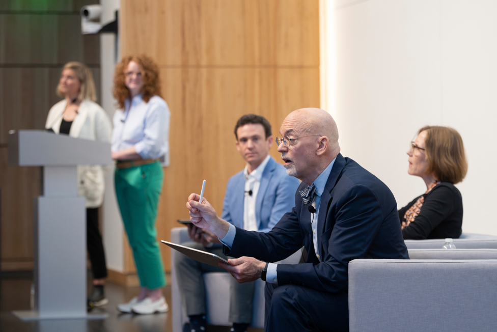A panel of two men and a woman speaking to an audience from stage.