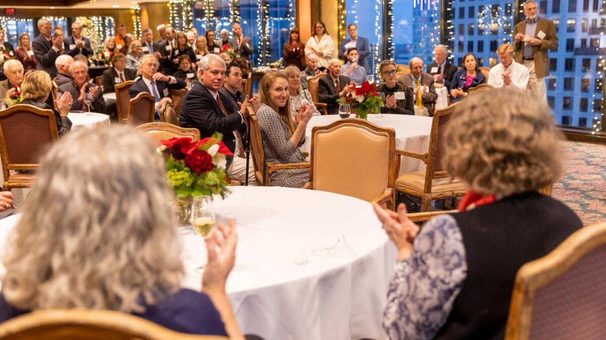 attendees seated at round tables applaud during holiday anniversary event